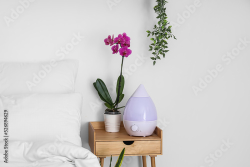 Fototapeta Naklejka Na Ścianę i Meble -  Orchid flower and humidifier on bedside table near white wall