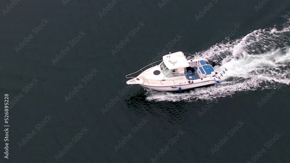A white motorboat cruising along calm water at a fast speed - aerial follow