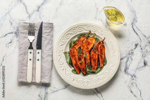 Plate of tasty baked carrots with greens, oil and cutlery on light background