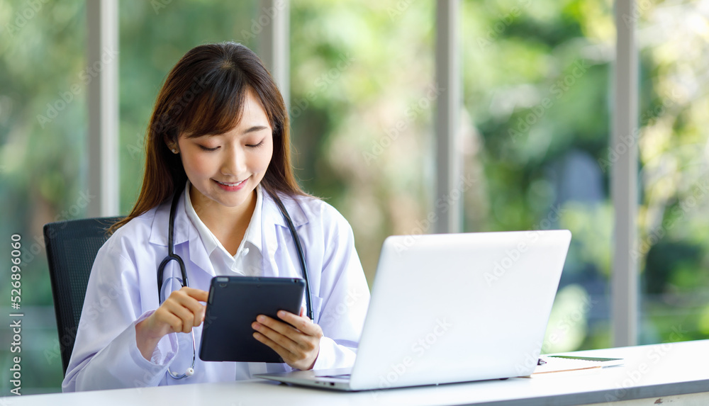 Asian successful professional young female doctor in white lab coat uniform with stethoscope sitting smiling using typing laptop notebook computer working researching online in hospital clinic office Asian successful professional young female doctor in white lab coat uniform with stethoscope sitting smiling using typing laptop notebook computer working researching online in hospital clinic office