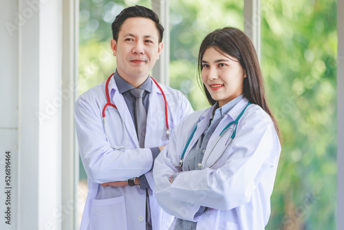 Asian young cheerful professional male and female intern practitioner doctor colleague in white lab coat uniform with stethoscope standing smiling together holding patient paperwork document folder