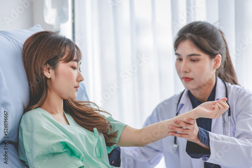 Wallpaper Mural Asian young professional female practitioner doctor in white lab coat with stethoscope holding touching checking monitoring patient injury arm and muscle while laying down on bed in hospital wardroom Torontodigital.ca