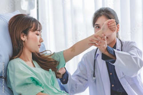 Wallpaper Mural Asian young professional female practitioner doctor in white lab coat with stethoscope holding touching checking monitoring patient injury arm and muscle while laying down on bed in hospital wardroom Torontodigital.ca