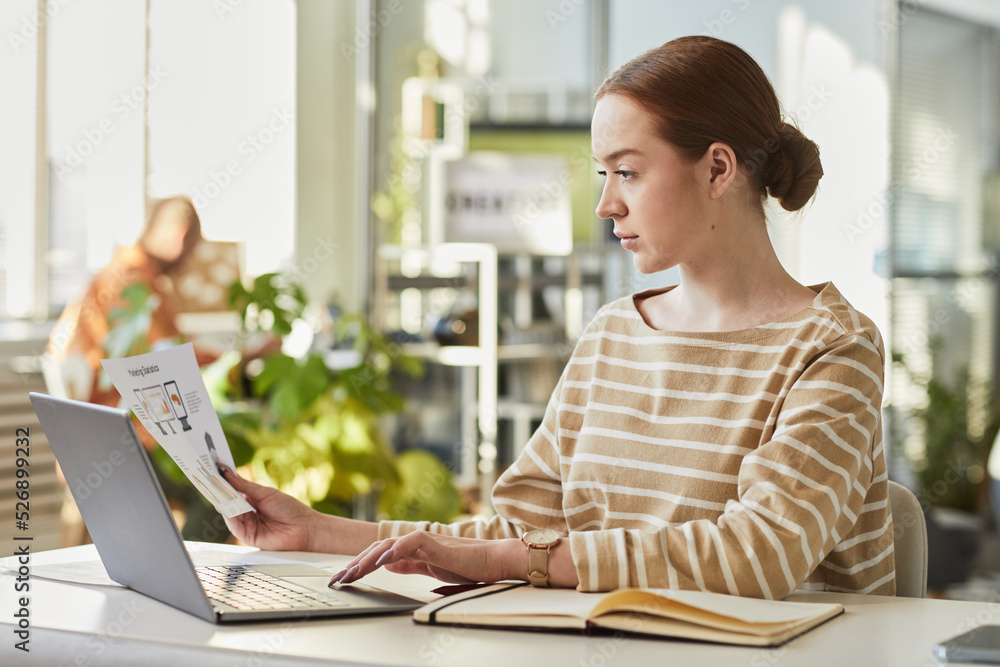 Minimal side view portrait of young Caucasian woman working with laptop at office workplace and analyzing marketing data, copy space Minimal side view portrait of young Caucasian woman working with laptop at office workplace and analyzing marketing data, copy space