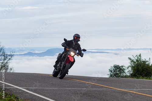 Motorcyclist riding a motorcycle on a paved road behind the sea of fog and mountain peaks, Mo Hin Khao, Chaiyaphum Province, Thailand. photo