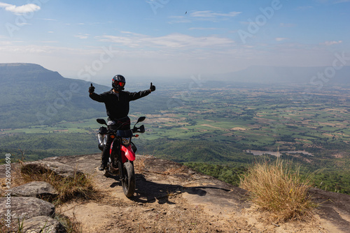 A motorcyclist parked his motorcycle on a high cliff. Below are mountains and green trees, a thousand-year-old forest, Chaiyaphum Province, Thailand.