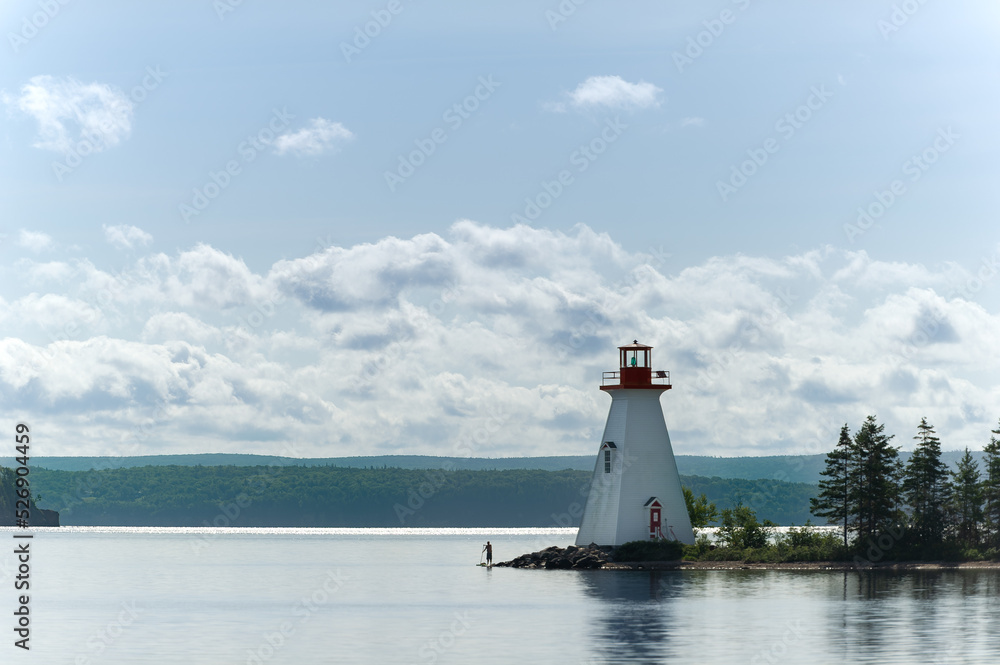 Sunrise view of lighthouse on Bras D'Or lake near Baddeck, Nova Scotia Canada. Silhouette of a person paddle boarding passing near the lighthouse.
