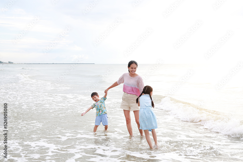 Asian mother and kids enjoy playing on tropical sand beach at sunrise. Happy family mom and child having fun in summer holiday.