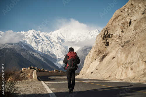 asian hiker backpacker walking on highway with snow mountain in background