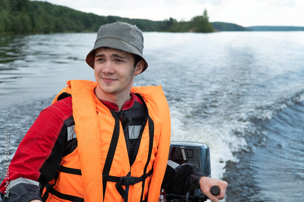 A young attractive man in a red life jacket is driving a motorboat A young attractive man in a red life jacket is driving a motorboat