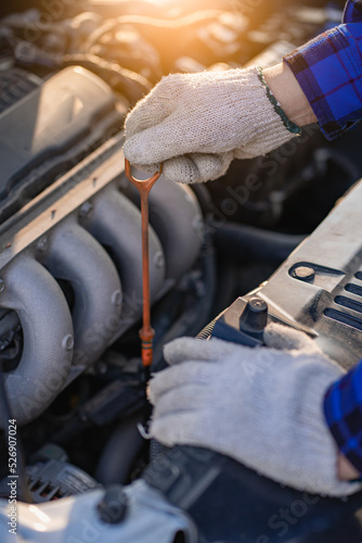 of a young man wearing white gloves checking the oil level of a car with a dipstick, close-up