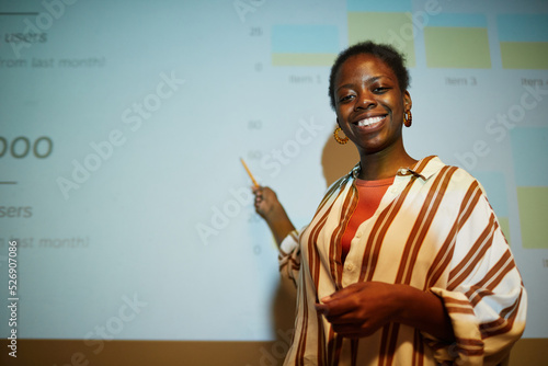 Fotografiet Waist up portrait of black young woman giving presentation on by projector scree