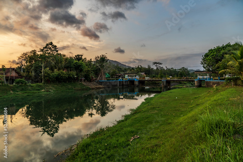 Colorful sunset, sunrise over a wide river. Twilight rays and clouds reflected in the calm water in Trenggalek village, East Java, Indonesia