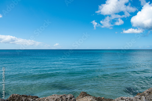 A view of the ocean from rocks. The sky is blue with some white clouds.