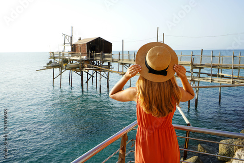 Romantic sunset in Italy. Back view of young woman with hat and dress enjoying view of Trabucco an old fishing machine on Adriatic Sea, Italy. photo
