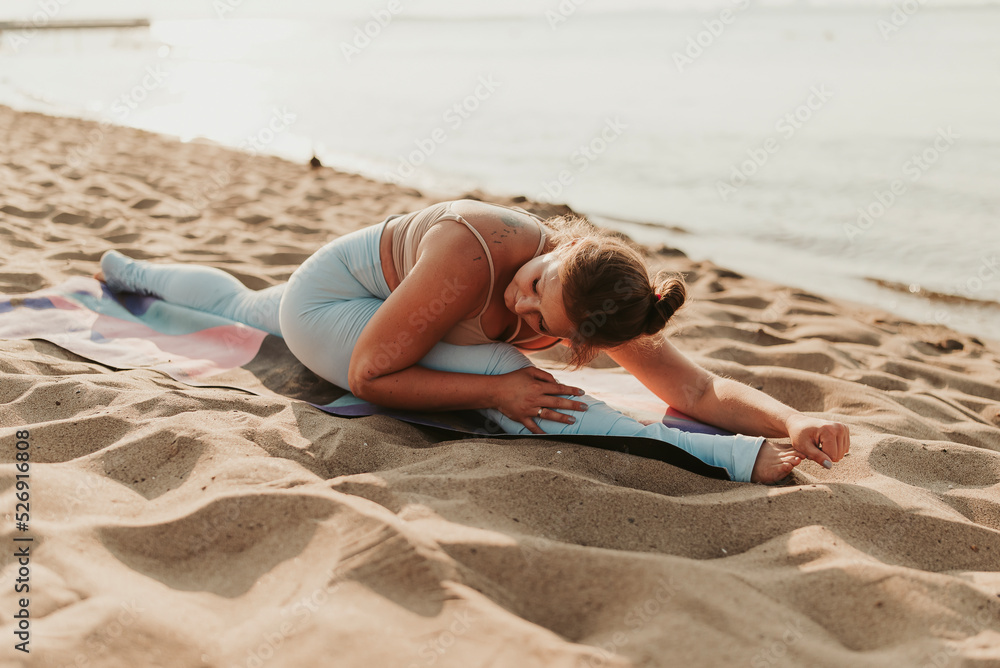 Caucasian woman practicing yoga at seashore sandy beach on sunrise. Womens health and wellness. Sports body positive. Real instructor poses Caucasian woman practicing yoga at seashore sandy beach on sunrise. Womens health and wellness. Sports body positive. Real instructor poses