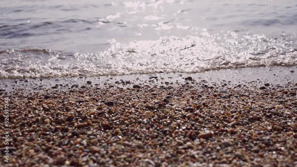 Close-up of pebble beach with transparent waves with sun glare on the water. Close up of stony sea shore. Natual background of calm sea in the surf zone. Camera moves sideway to the right side Close-up of pebble beach with transparent waves with sun glare on the water. Close up of stony sea shore. Natual background of calm sea in the surf zone. Camera moves sideway to the right side