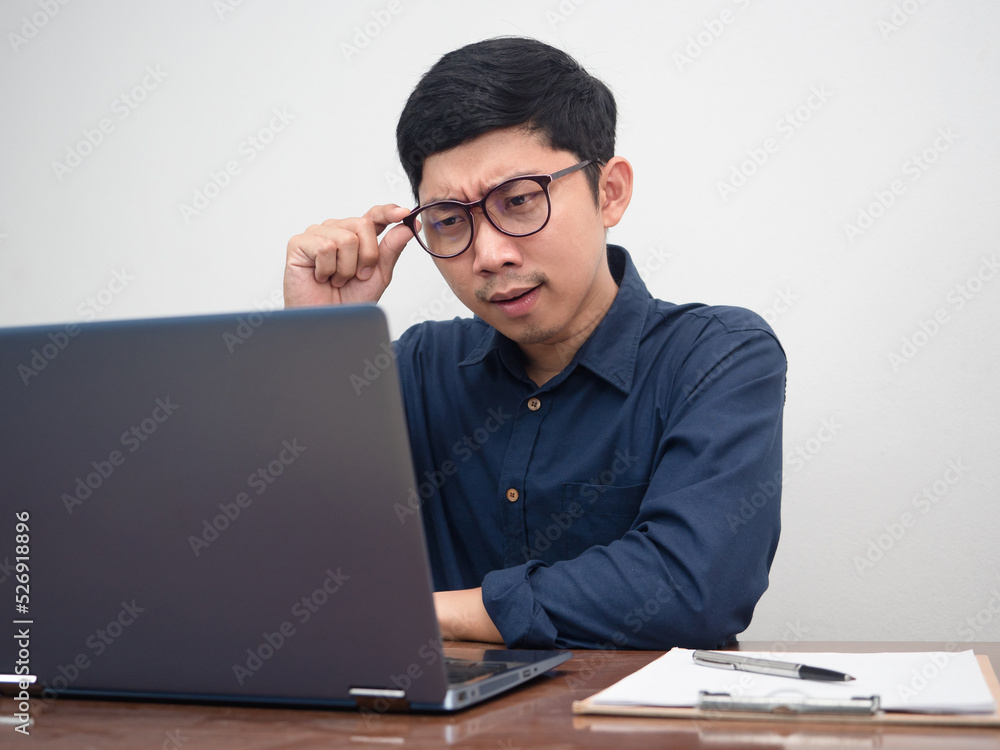 Asian man wear glasses looking at laptop on workplace table Asian man wear glasses looking at laptop on workplace table