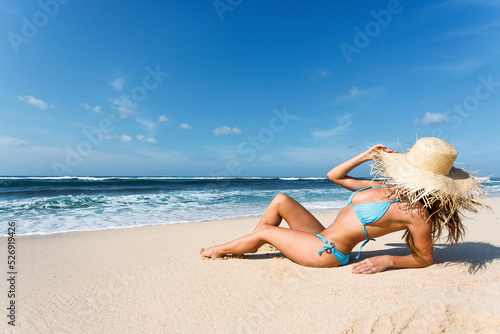 Valokuva Woman in blue swimsuit and wide brim hat on tropical beach sunbathing and relaxi