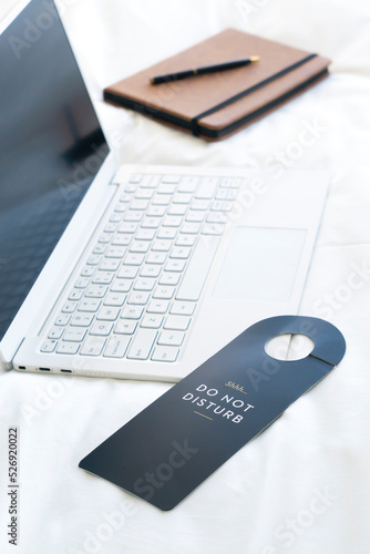 Close-up of do not disturb sign with laptop in bed