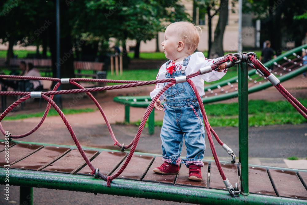 A little girl in an embroidered shirt and denim jumpsuit plays on the playground A little girl in an embroidered shirt and denim jumpsuit plays on the playground