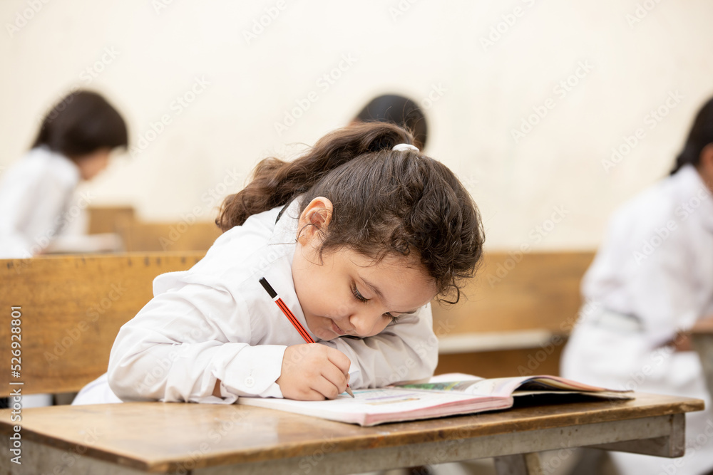 Happy Indian elementary schoolgirl students sitting at desk in classroom with writing in notebook with pencil, Examination and test, female Education concept. Happy Indian elementary schoolgirl students sitting at desk in classroom with writing in notebook with pencil, Examination and test, female Education concept.