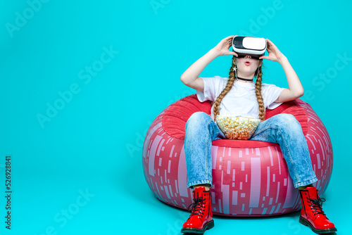 Virtual Technology Ideas. Winsome Teenage Female in White Shirt Posing in Modern Virtual Reality VR Helmet With Popcorn And Excited Expression On Trendy Turquoise Background. photo