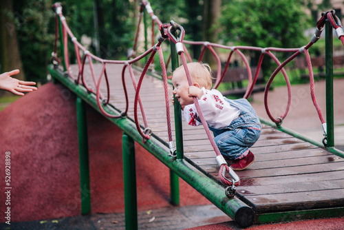 A little girl in an embroidered shirt and denim jumpsuit plays on the playground