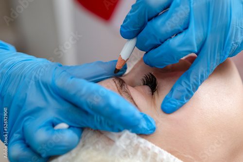 Closeup of An Eye of Caucasain Female During Tattoo Facial Markings Using Black makeup Pencil During Professional Eyebrow Permanent Makeup in Salon.