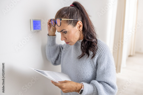 Woman standing next to a thermostat cannot believe the price for heating on her bill due to energy crisis in Europe photo