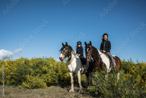 Portrait mother and daughter horseback riding in sunny rural field
