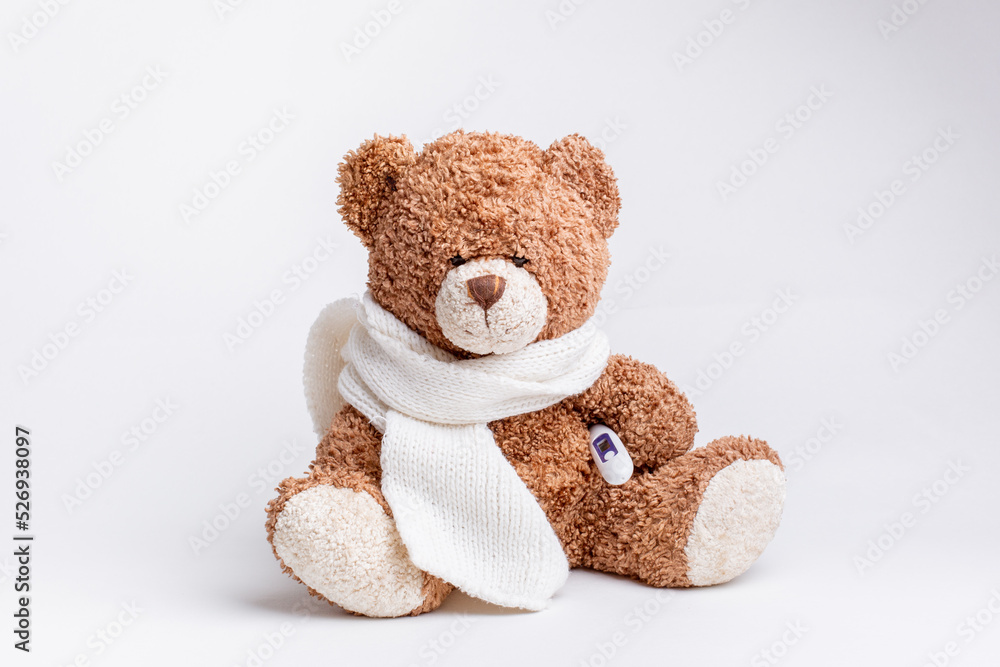Obraz premium a teddy bear with a thermometer and a knitted scarf is sick on a white background, isolated