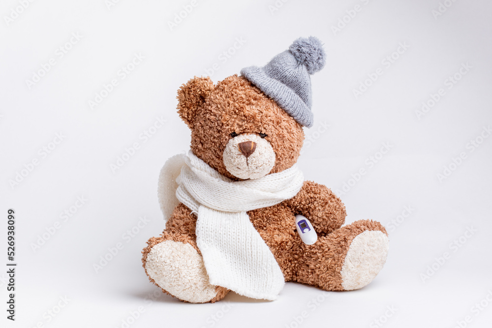 a teddy bear with a thermometer and a knitted scarf and hat is sick on a white background, isolated a teddy bear with a thermometer and a knitted scarf and hat is sick on a white background, isolated
