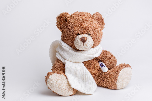 a teddy bear with a thermometer and a knitted scarf is sick on a white background, isolated