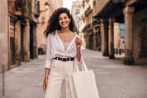 Positive young african female looks at camera stands on street with shopping bags. Model wears casual clothes. Concept fashion, good mood. © Look!