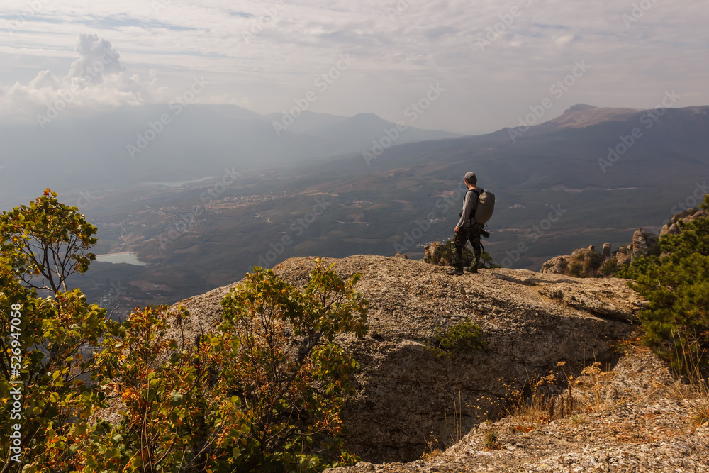 A tourist stands on the rock of the Demerdzhi mountain range with a view of the valley