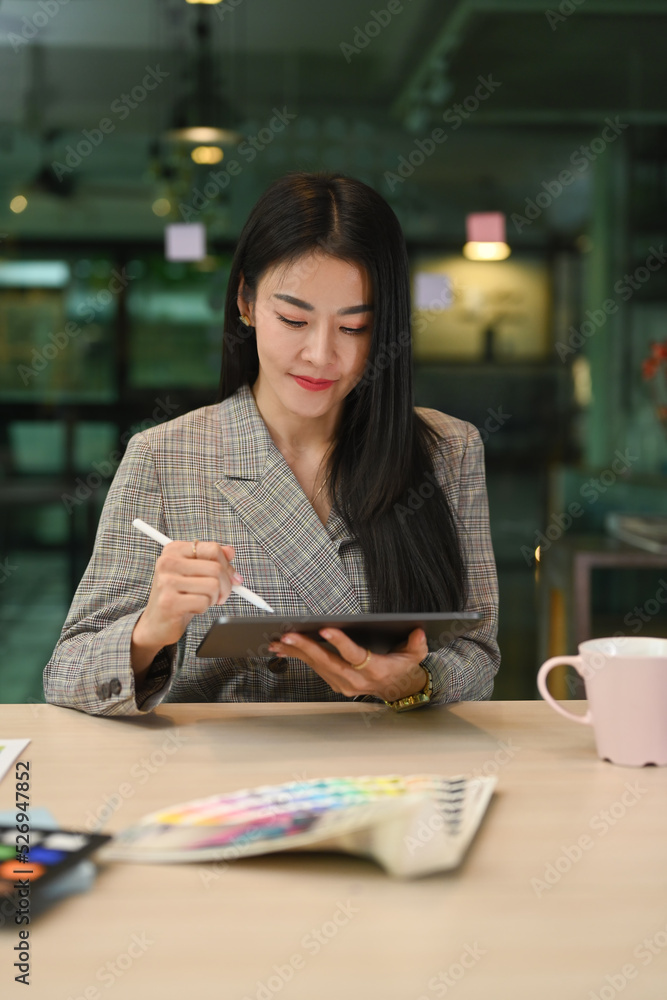 Attractive millennial woman working on new creative project with color swatches and digital tablet at creative office Attractive millennial woman working on new creative project with color swatches and digital tablet at creative office