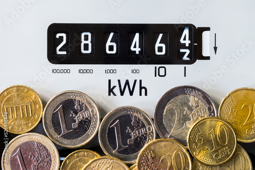 Close-up of electric meter and Euro coins. Focus on kWh symbol. Concept for global energy crisis, cost of living, high electricity prices, power, heating and higher bills.