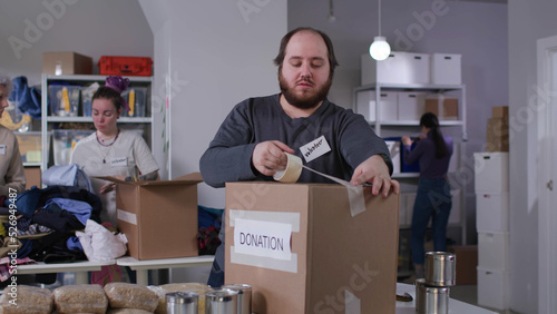 Overweight volunteer use tape packing donated food in boxes working in military center © TommyStockProject