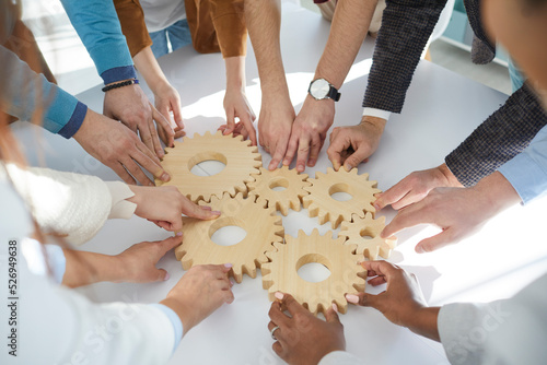 Close up of wooden gears that business people connect together during teambuilding session. Male and female colleagues together find business solutions and contribute to development of business.