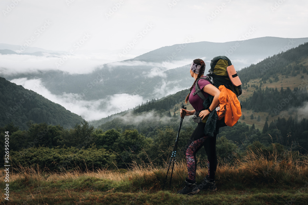 Woman hiking with backpack and trekking poles on summer day. Nature tourism in Ukrainian Carpathian mountains.
