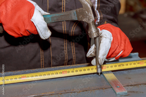 The worker uses a Center Punch and a hammer to mark the iron surface.