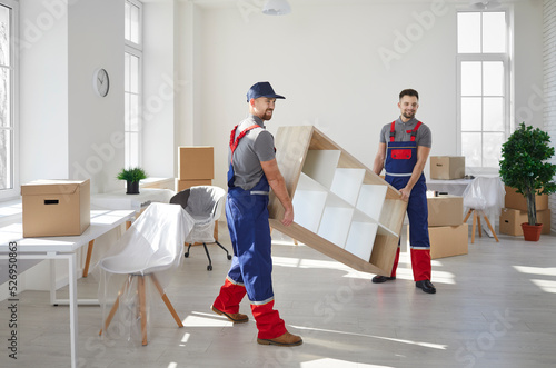 Male movers in uniform carry furniture help client with office or home settle. Deliverymen or carriers work for customer during moving or relocation. Delivery or transportation company service.