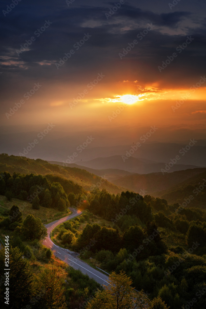 Beautiful summer mountain landscape, clouds and sun rays at sunset. Road in the mountains at sunset. Vertical shot
