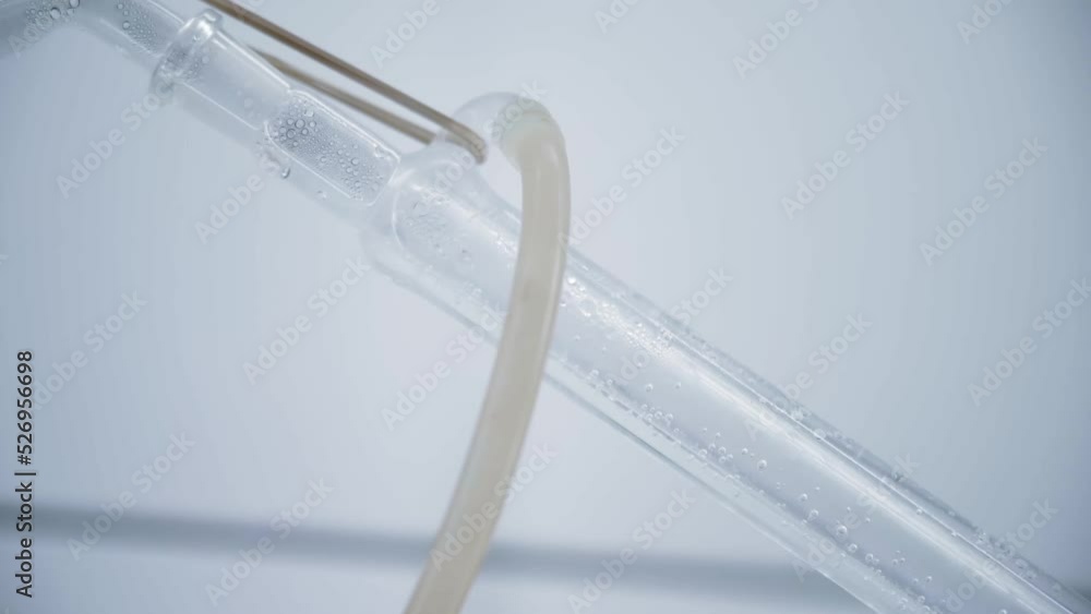 Clear drops flow down the tube. Camera moves slowly along the tube. Distillation process. Flasks in a bright laboratory. Chemical reaction. 4K Clear drops flow down the tube. Camera moves slowly along the tube. Distillation process. Flasks in a bright laboratory. Chemical reaction. 4K