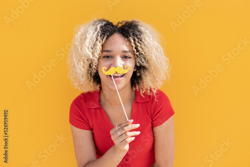 Happy woman with mustache prop in front of yellow wall