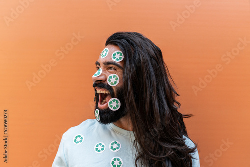 Shouting bearded man with recycling stickers on face in front of wall photo