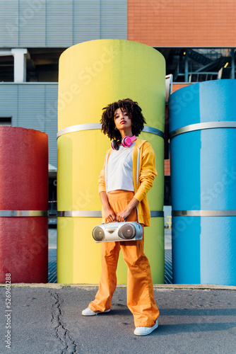 Young woman holding boom box standing in front of colorful pipes