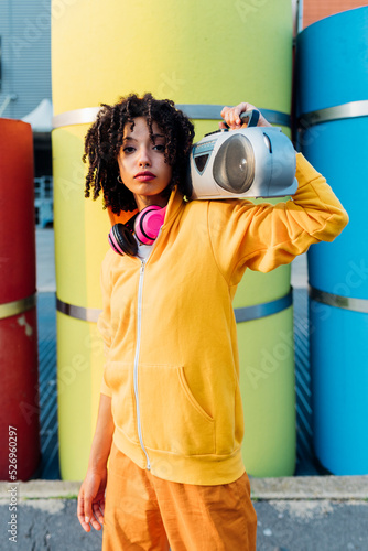 Woman carrying boom box on shoulder standing in front of colorful pipes