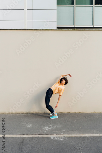 Woman with hand raised bending over backwards in front of wall
